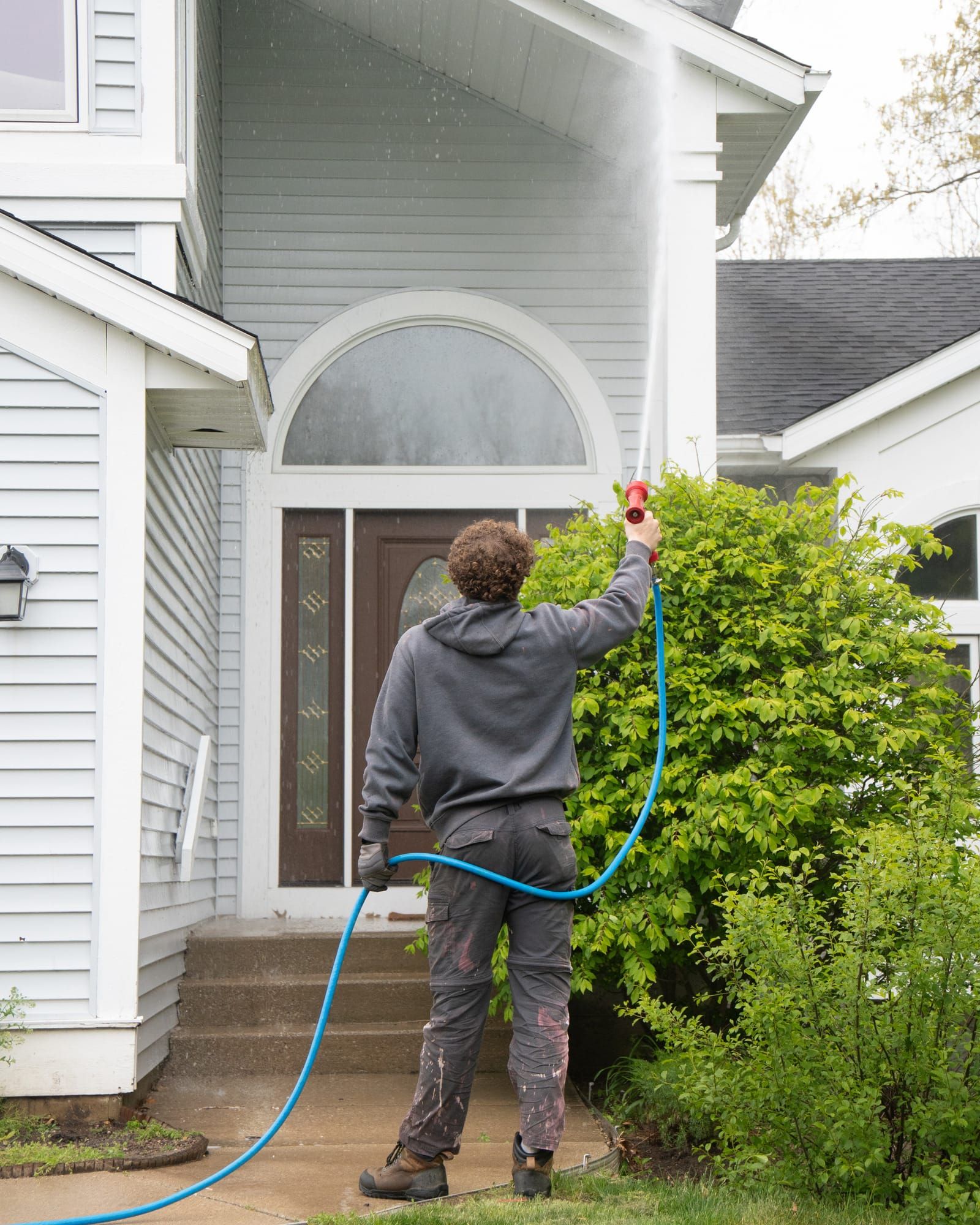 Elevation technician soft-washing the gable and eave above a home's arched front entry