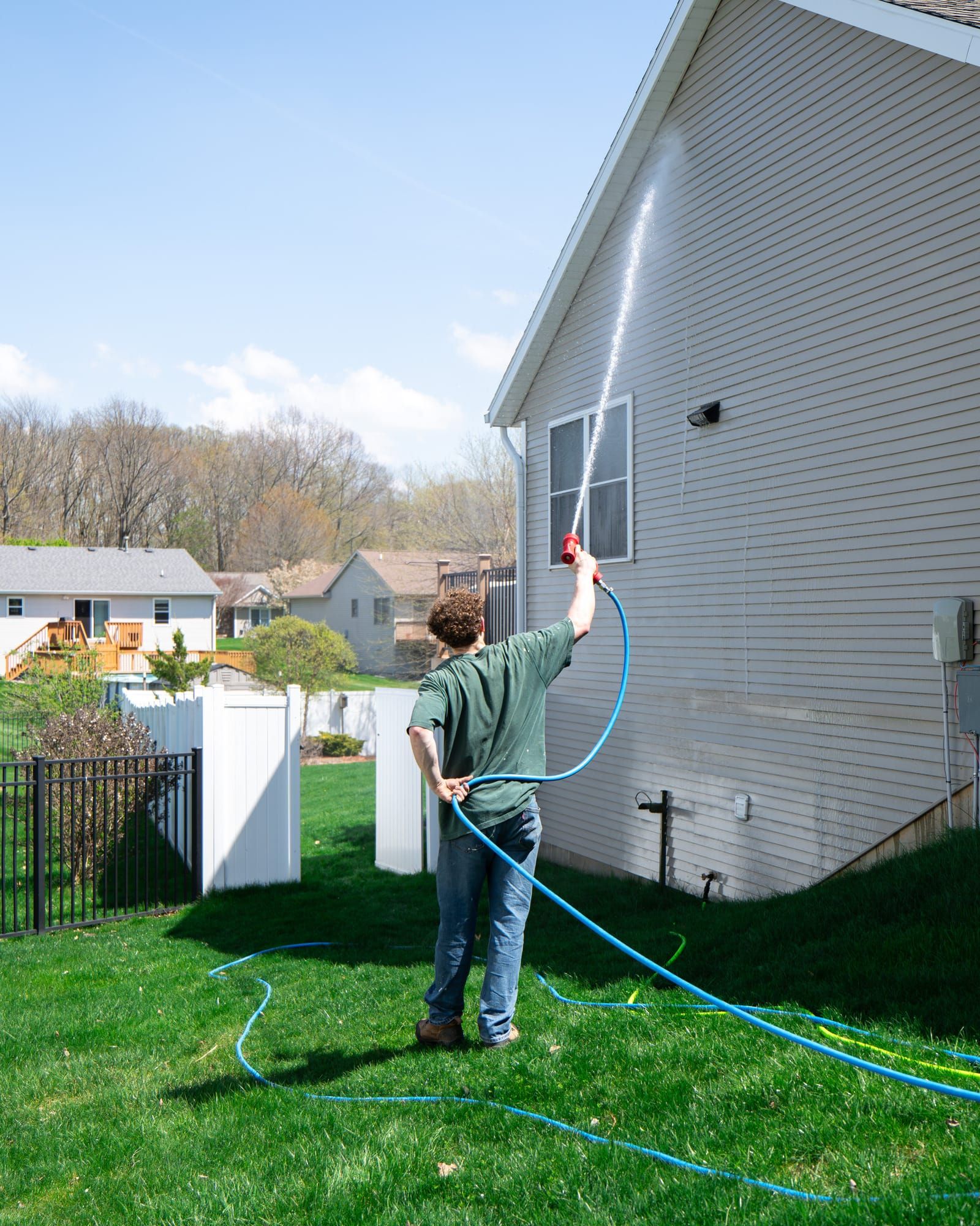Elevation technician soft-washing the gable end of a two-story home from ground level with a low-pressure spray